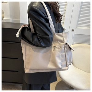 Detail of beige canvas tote bag showing side flap pocket and zipper front compartment