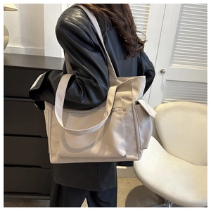 Detail of beige canvas tote bag with multiple pockets worn by a model in casual setting