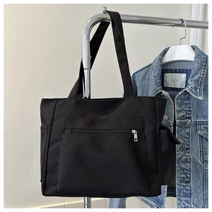 Detail of black canvas tote bag showing large front zipper pocket and side compartments
