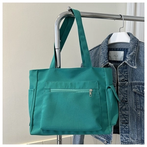 Detail view of large green canvas tote bag with functional zipper pocket and side slots