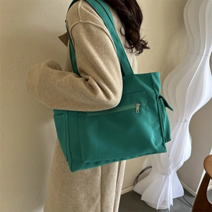 Green canvas tote bag with front zipper pocket shown in a stylish minimalist setting