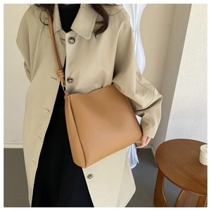 Tan leather tote bag with knotted strap detail styled with beige trench coat for commute