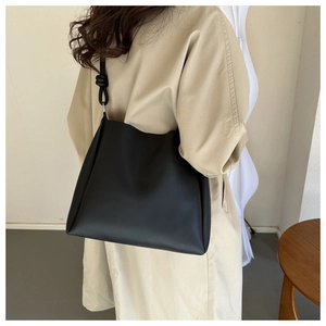 Close-up of a black minimalist matte leather tote bag featuring a unique knotted shoulder strap