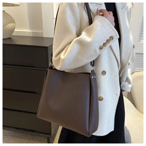 Detail of dark brown leather bucket bag with metal rivets on model in beige wool coat