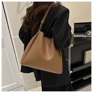Detailed view of brown PU leather tote bag with knotted shoulder strap on office background