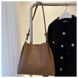 Detail of brown tote bag with knotted strap and metal ring hanging on a hanger