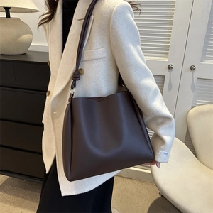 Minimalist dark brown leather bucket bag with knotted shoulder strap detail on model