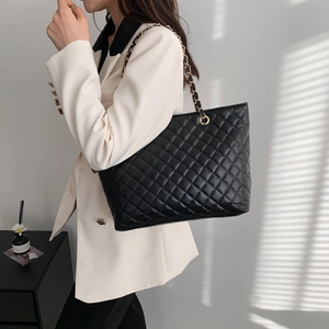 Quilted black tote bag with gold chain straps shown on model in natural sunlight