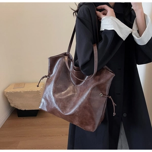 Détail d'un sac cabas en cuir marron foncé avec œillets métalliques et aspect brillant