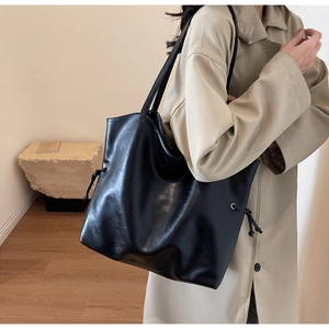 Side view of a large black faux leather tote bag with stylish drawstring details