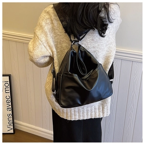 Détail d'un sac cabas en cuir noir porté en bandoulière sur un pull en maille beige