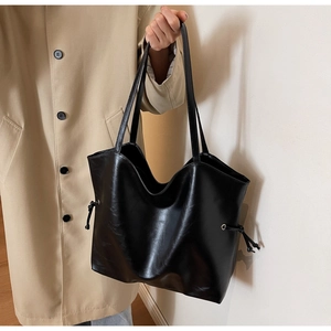 Close-up of black PU leather tote bag with side drawstring detail on beige trench coat