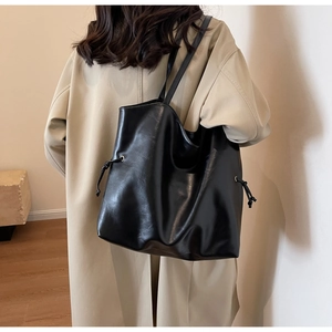 Detail of a large black tote bag featuring glossy leather and stylish side drawstring accents