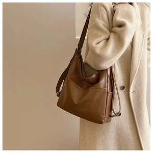 Sac hobo minimaliste en cuir marron caramel porté avec un manteau beige élégant