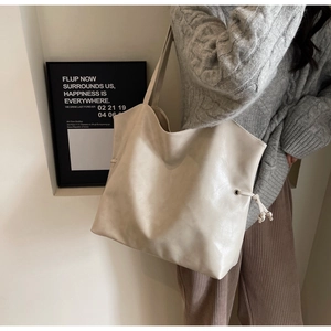 Detail of a large beige PU leather tote bag with side eyelets and drawstring decor