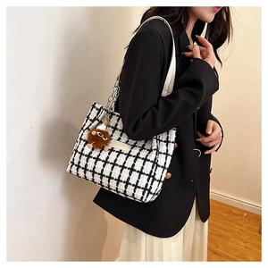 Detail of tweed checkered tote bag with leather strap and plush monster charm