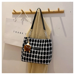 Detail of tweed checkered tote bag with brand label and cute plush monster charm