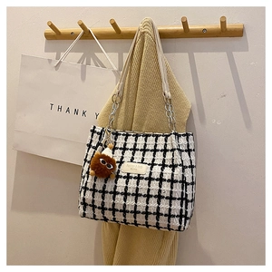 Detail of checkered tweed tote bag with metal chain strap and a plush charm on wood hook