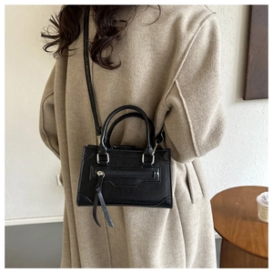 British style black leather crossbody bag with tassels shown on a beige wool coat