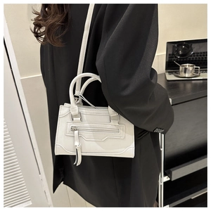 Close-up of white mini handbag with silver hardware and tassel worn by a model
