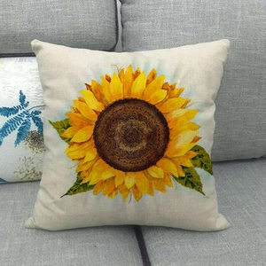 Close-up of a square linen cushion cover featuring a vibrant sunflower on a grey sofa