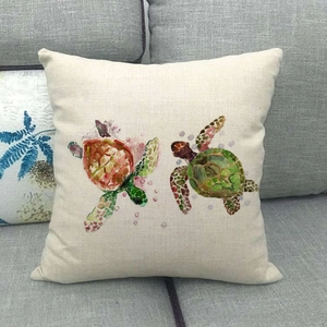 Detail of square linen pillow with watercolor sea turtle print on a grey fabric sofa