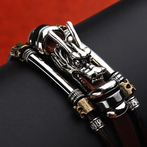 Detailed close-up of a carved silver dragon head pendant on a multi-layer leather bracelet