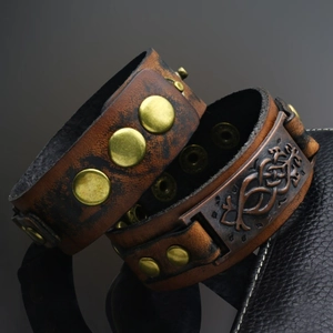 Close-up of vintage leather bracelet showing bronze rivets and Celtic knot engraving