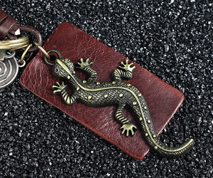 Detailed close-up of a vintage bronze gecko lizard keychain with leather tag on black stones