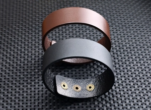 Detail van brede leren armbanden in bruin en zwart met gouden metalen klinknagels