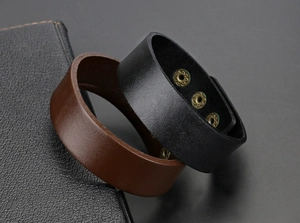 Detail van brede leren armbanden in zwart en bruin met vintage metalen drukknoppen