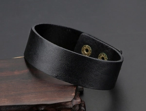 Macro-opname van zwarte brede leren armband met bronzen drukknopen op houten display