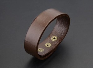 Detail van een bruine lederen brede armband met drie vintage gouden drukknopen