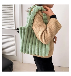 Detail of light green plush tote bag with unique fuzzy ball handles and striped texture