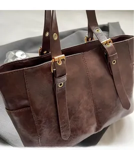 Detalle del bolso tote marrón oscuro con cuero de textura aceitosa y hebilla dorada