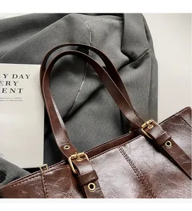 Detalle de bolso tote vintage marrón oscuro con hebilla dorada ajustable y costuras finas