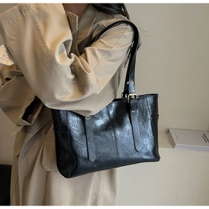 Detalle de bolso tote de piel sintética negra brillante con correas y herrajes dorados