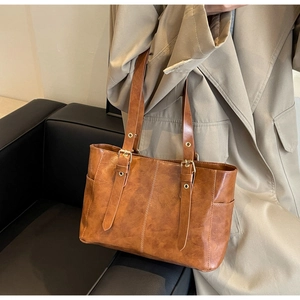 Detalle de bolso tote vintage marrón con textura de piel sintética y hebillas metálicas finas