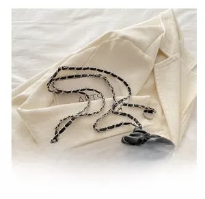 Détail de ce sac seau noir matelassé avec bandoulière chaîne porté sur un blazer crème élégant