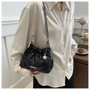 Gros plan d'un sac seau matelassé noir avec bandoulière chaîne et pendentif logo