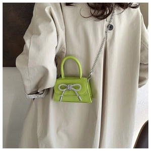 Detail of neon green mini bag with rhinestone bow and silver chain on model