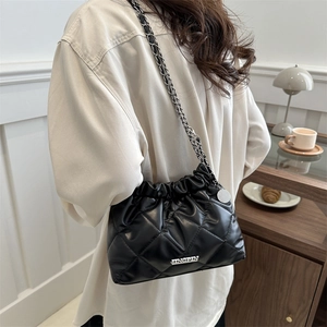 Sac seau matelassé noir avec bandoulière chaîne présenté dans un café chaleureux