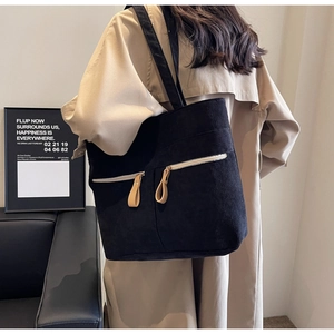 Detail of black corduroy tote bag with dual front zipper pockets on beige coat model