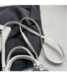 Detail of light blue denim handbag featuring contrast white shoulder straps and silver hardware