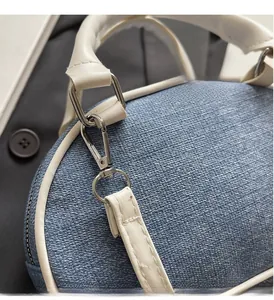 Detailed shot of silver hardware and stitching on blue denim with white leather trim