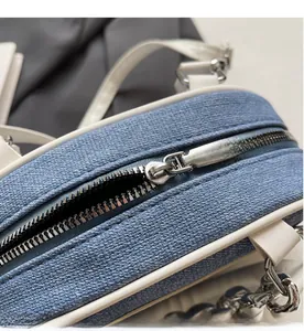 Close-up of smooth silver metal zipper on blue denim bag with white piping detail