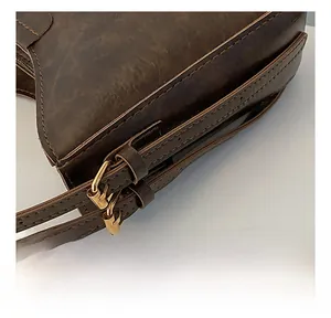 Détail de la bandoulière réglable avec boucles en métal doré sur un sac seau en cuir marron
