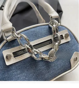 Detail of denim canvas handbag showing shiny silver metal chain and leather trim textures