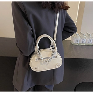 Vue détaillée du sac crème semi-ovale avec chaîne argentée porté sur un blazer sombre