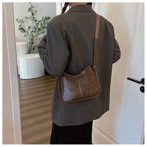 Détail du sac seau marron foncé avec cuir texturé et large bandoulière en tissu tressé